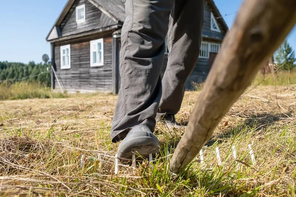 Gamba di un uomo negligente e disattento passi su un rastrello, che può portare a lesioni, sullo sfondo di una casa di villaggio e cortile, — Foto Stock