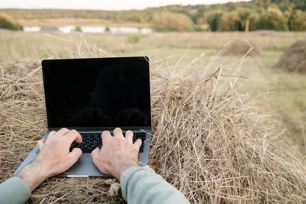 Fernbedienung mit einem Laptop auf einem Heuhaufen, vor dem Hintergrund einer wunderschönen ländlichen Landschaft, an einem Sommerabend. Lebensstil. — Stockfoto