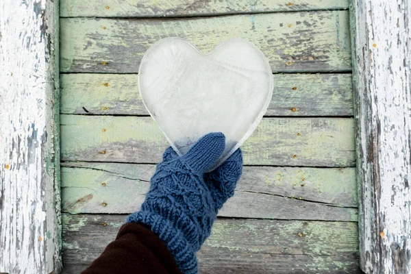 Hari Valentine. Hati, simbol cinta, terbuat dari es, dipegang oleh tangan dengan sarung tangan terhadap latar belakang dinding kayu tua. — Stok Foto