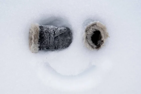 Zabawna, domowej roboty buźka, z rękawiczkami zamiast oczu i malowanym uśmiechem na śniegu. Kreatywny pomysł. Widok z góry. — Zdjęcie stockowe