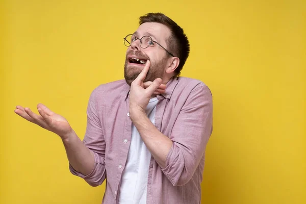 Perplexed man in glasses and casual clothes opened his mouth, shows a missing tooth and makes an inquiring gesture with hand. — Stock Photo, Image