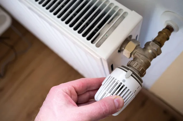 Mão transforma o termostato do radiador para o mínimo, devido ao aumento dos preços do gás. Conceito de crise energética e economia. — Fotografia de Stock