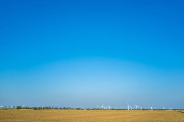 Tarım arazisi, tarla sürülmüş, mavi gökyüzüne ve rüzgar türbinlerine karşı. Harika kırsal alan, bahar günü..