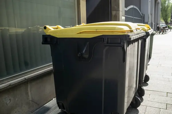 Contenedores de basura de plástico están cerca de los edificios escaparate, en una calle de la ciudad, en un día de primavera. — Foto de Stock