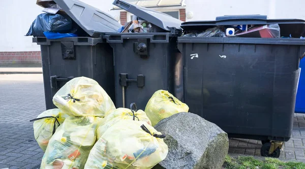 Overflowing plastic garbage containers and waste package lie on a city street.