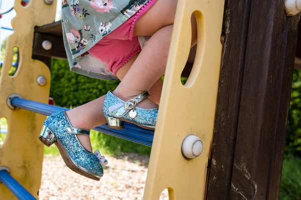 Jambes d'un enfant dans de belles chaussures brillantes avec des talons, en short et une robe monter les escaliers sur l'aire de jeux. Gros plan. — Photo