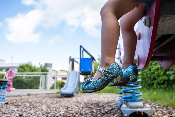 Ноги ребенка в красивых туфлях на высоких каблуках сидят и отдыхают на качелях, на детской площадке, на открытом воздухе. — стоковое фото