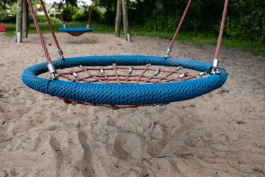Wicker salıncağı, kumlu yüzeyi olan özel donanımlı bir oyun parkında asılı, açık havada, bir yaz gününde..