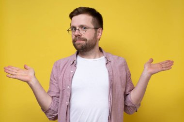 Gözlüklü yakışıklı beyaz adam hoş bir sürprizle karşılaşıyor, kollarını açıyor ve hayret içinde bakıyor. İzole edilmiş, sarı arkaplan.