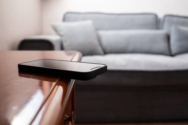 Akıllı telefon ahşap bir çekmecenin kenarına dikkatsizce bırakılır ve düşebilir. Olaylara dikkatsiz yaklaşma kavramı.