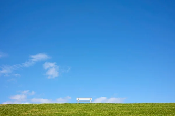 Holzbank Auf Einem Grünen Hügel Vor Blauem Himmel Und Wolken lizenzfreie Stockbilder