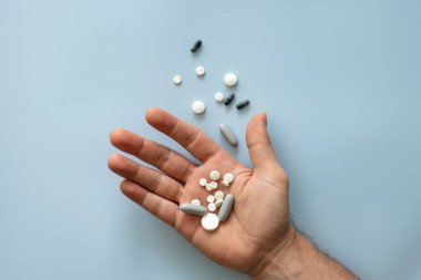 Bir avuç dolusu hapın ve mavi arka planda dağınık ilaçların olduğu bir avuç dolusu yakın plan. Soğuk mevsime ya da uyuşturucu bağımlılığına hazırlık kavramı. Üst görünüm. 