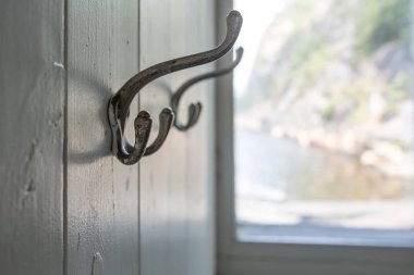 Giysiler için iki eski metal kanca, ahşap bir duvarda, pencerenin arka planında, içeride. Yakın plan..