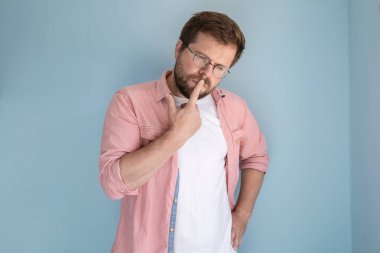 Düşünceli genç adam parmaklarını ağzında tutuyor ve üzgün bir şekilde mavi bir arka plana bakıyor..