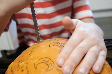 Cadılar Bayramı hazırlığı. Çizgili tişörtlü bir çocuk evde yerde otururken balkabağını balkabağına oyuyor. Yakın plan.. 