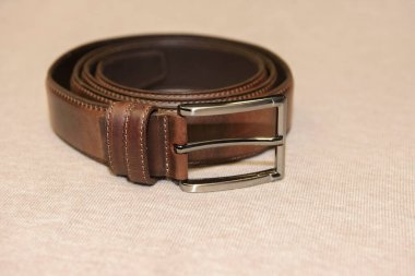 Kahverengi bir erkek deri kemeri bej bir arka planda yatıyor..