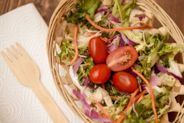 Hasır bir tabakta salatalı kırmızı kiraz domatesleri. Vejetaryen yemeği taze marul, roka, havuç, kırmızı lahana ve domates.