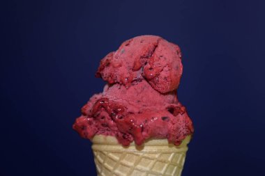 Berry red ice cream close-up. A child's hand holds a delicious ice cream cone on a blue background.
