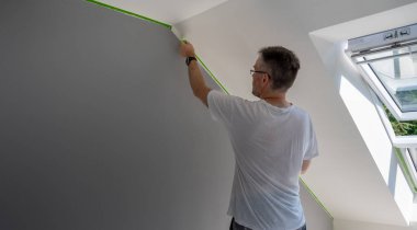 Painter removes masking tape and creates a sharp border between a grey and white painted part of a wall. 