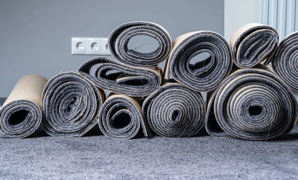 Stacked old carpet rolls in a grey room.