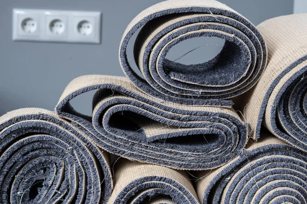 Stacked old carpet rolls in a grey room.