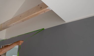 Painter removes masking tape and creates a sharp border between a grey and white painted part of a wall.	