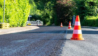 Construction cones marking part of road with a layer of fresh asphalt.	