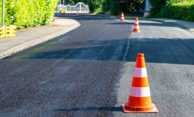 Construction cones marking part of road with a layer of fresh asphalt.	