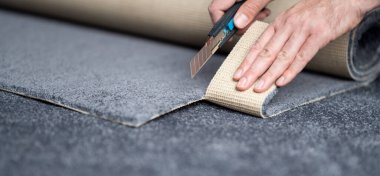 Handyman cutting a new carpet with a carpet cutter.	