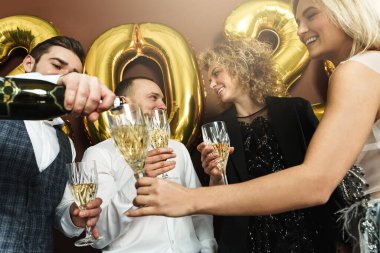 Bir grup güzel giyimli parti insanı yeni yılı kutluyor ve köpüklü şarap içiyor.