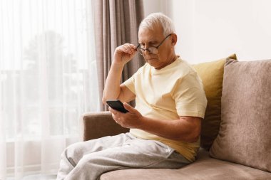 Gözlüklü adam evde akıllı telefon kullanıyor.