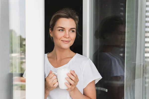 Genç Güzel Bir Kadın Elinde Bir Fincan Sıcak Kahveyle Pencereden — Stok fotoğraf