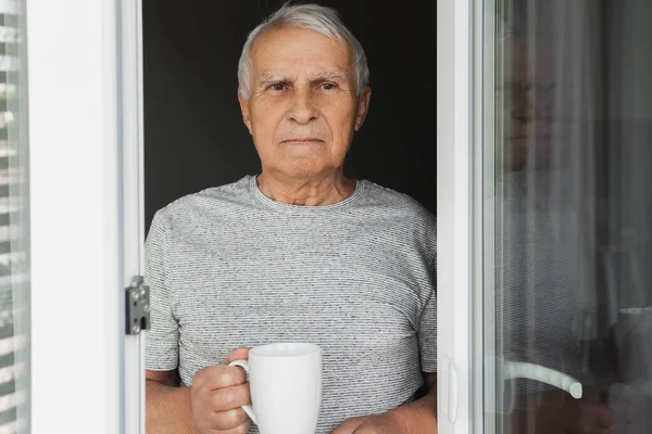 Elinde Bir Fincan Sıcak Kahveyle Pencereye Bakan Yaşlı Bir Adam — Stok fotoğraf