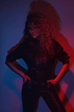 Genç ve seksi bir kadın şık Afro saç stili deri motosiklet giyip renkli neon ışıkta poz veriyor.