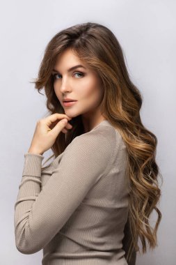 Gri arka planda kıvırcık saçlı güzel bir kadının portresi.