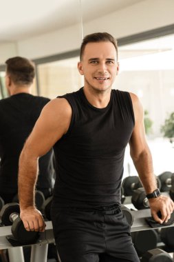 Modern spor salonunun serbest ağırlık bölgesinde genç bir adamın portresi.