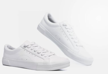 Gri arka planda bir çift beyaz deri spor ayakkabı.