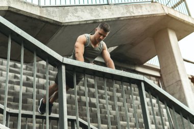 Genç ve kaslı bir adam, sokakta antrenman yaparken şınav çekiyor.