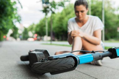 Şehrin caddesinde e-scooter sürerken geçirdiği kazadan sonra diz ağrısı çeken genç bir kadın.