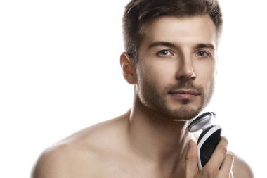 Genç ve yakışıklı adam beyaz arka planda modern elektrikli tıraş makinesi kullanıyor.