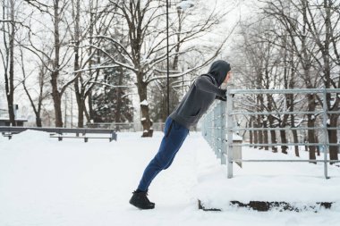 Sporcu adam kış antrenmanı sırasında karlı parkta şınav çekiyor.