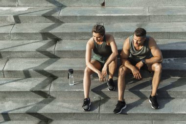 Genç atletik çift, koşudan ya da dışarıda spor yaptıktan sonra beton merdivenlerde oturuyor.