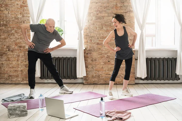 Two active elderly people during fitness workout with an online class at home.