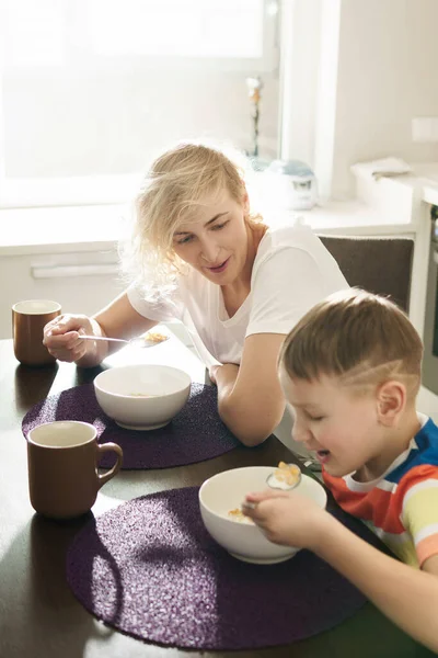 美丽的母亲和可爱的儿子在阳光灿烂的早晨吃着健康的玉米片当早餐 — 图库照片