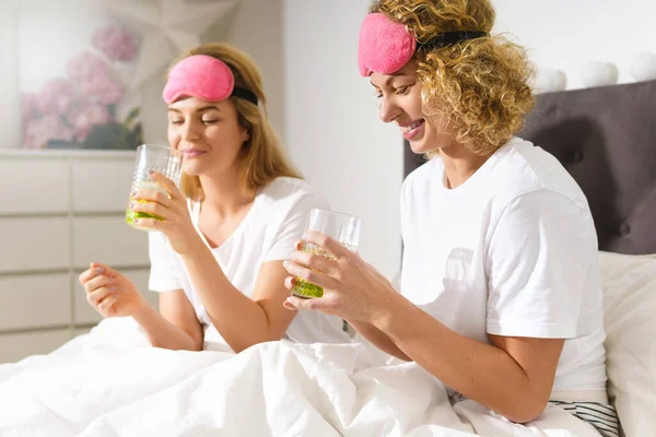 二人の美しいと陽気な女性はデトックス水を飲んで 快適なベッドで目覚めた後にチャット — ストック写真