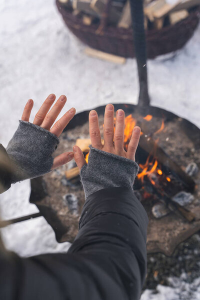Woman warming up her hands by the fire pit during cold winter day