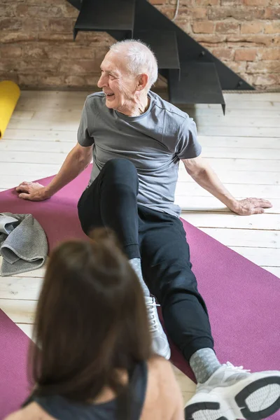 Two active elderly people sitting on a exercising mats during fitness workout at home