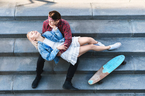 Top view of stylish teenage couple with a longboard is sitting on a concrete stairs