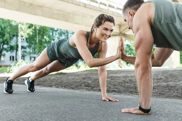 Atletik çift ve açık havada spor eğitimi. Erkek ve kadın, sokak egzersizi sırasında göğüs ve triseps kasları için şınav çekiyorlar. 