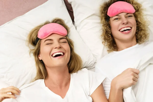 两个漂亮而快乐的女孩 戴着粉色的眼罩躺在床上 躺在床上休息 — 图库照片